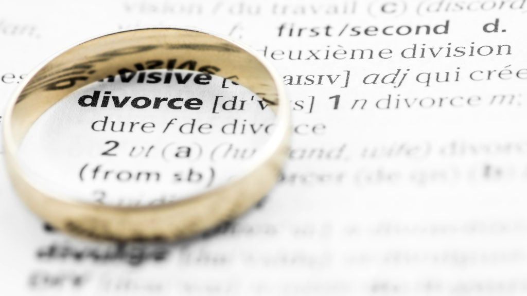 Divorce term text in macro from dictionary book, highlighted word with a gold wedding ring placed on printed white paper page. Concept of family, relationship difficulties, wedding and divorce.